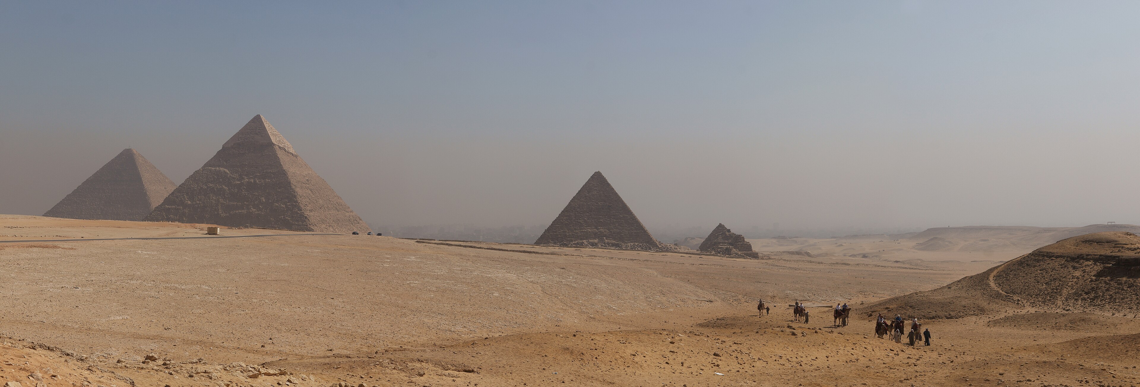 The three pyramids of Giza rising from the desert on the edge of Cairo, with a camel caravan crossing the sand.