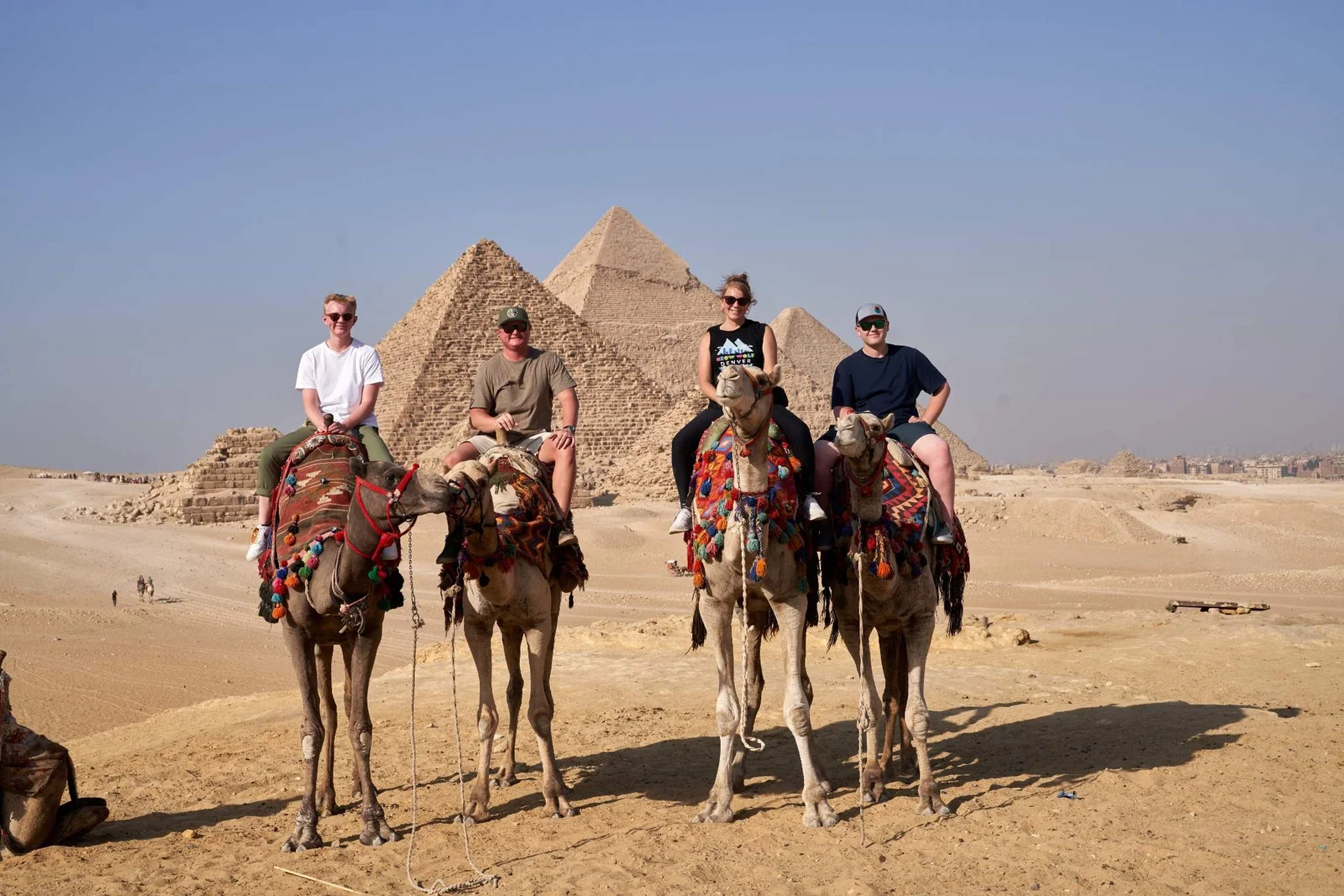 Four travelers on camels in front of the Pyramids of Giza