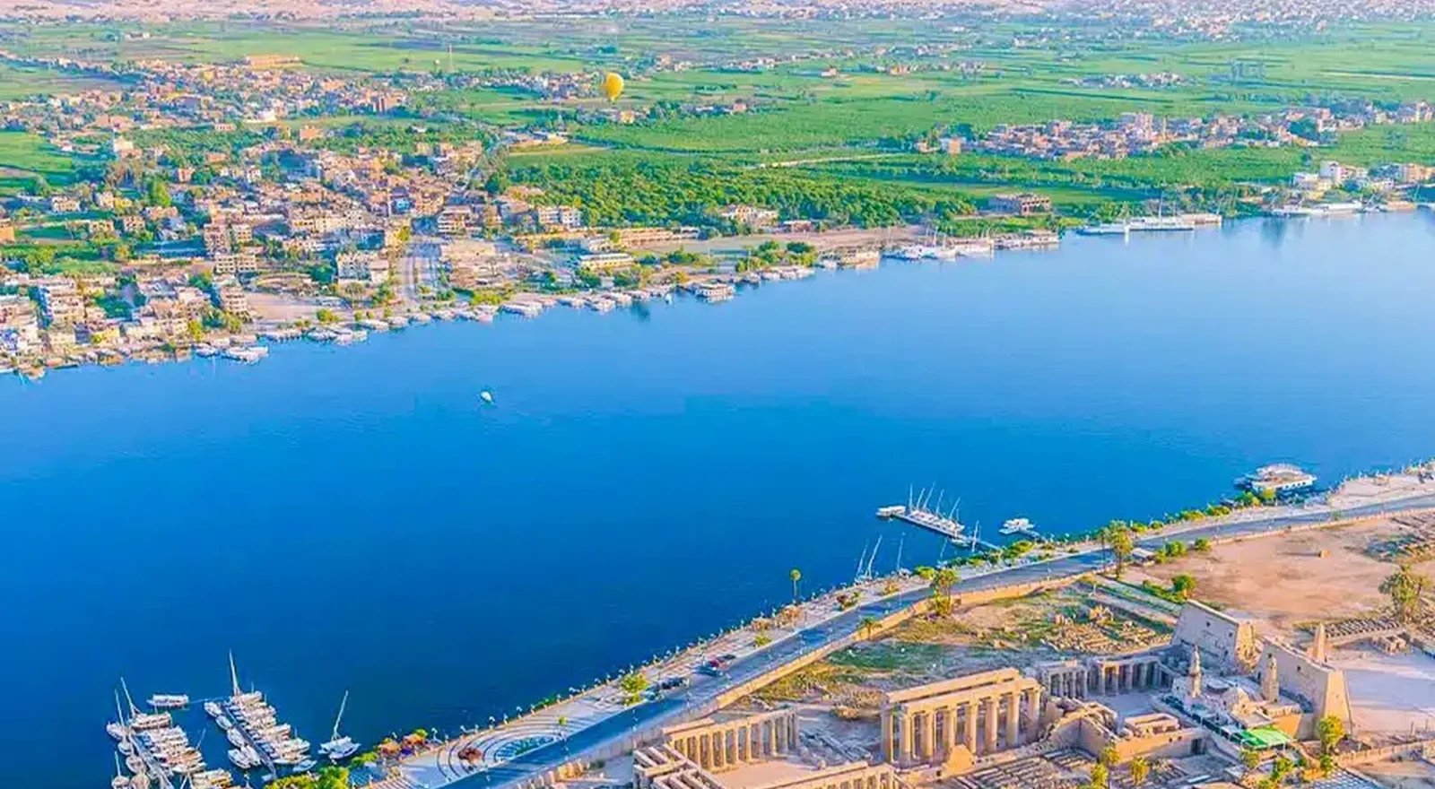 Vista aérea del Nilo a su paso por Luxor, con el templo de Luxor en la orilla y un globo aerostático al fondo