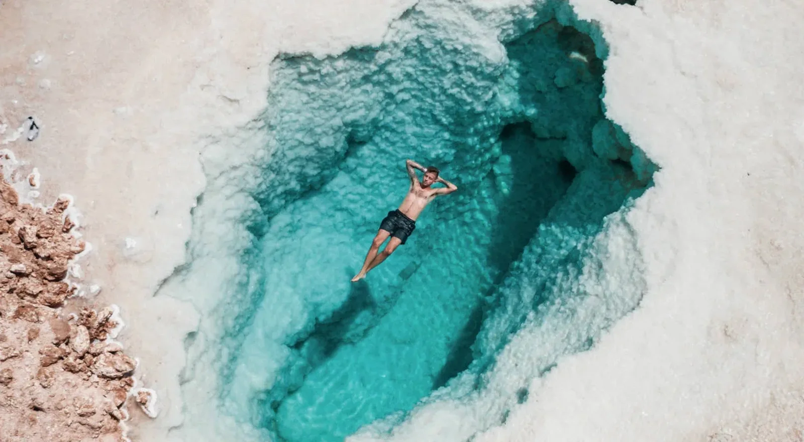 Una persona flota en una poza de agua turquesa rodeada de sal en el oasis de Siwa
