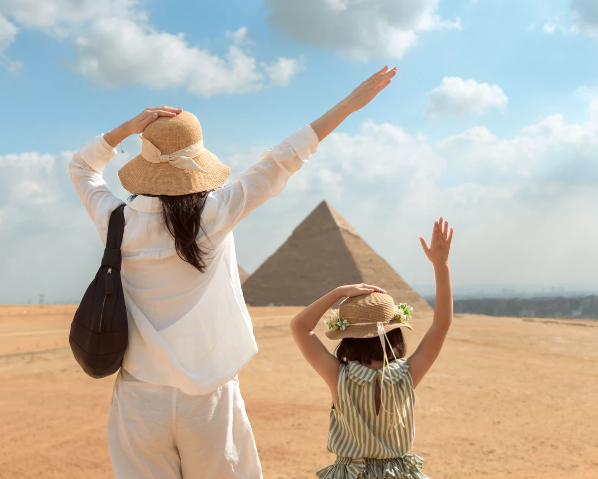 A tourist and her daughter taking a photo from behind in front of the pyramids