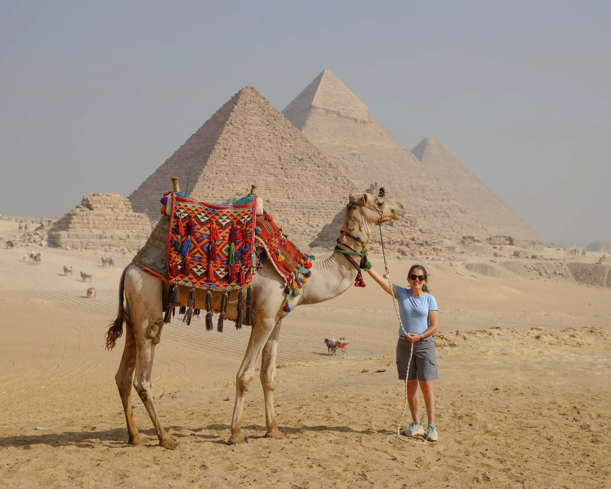 A tourist taking photos with camels in front of the pyramids.