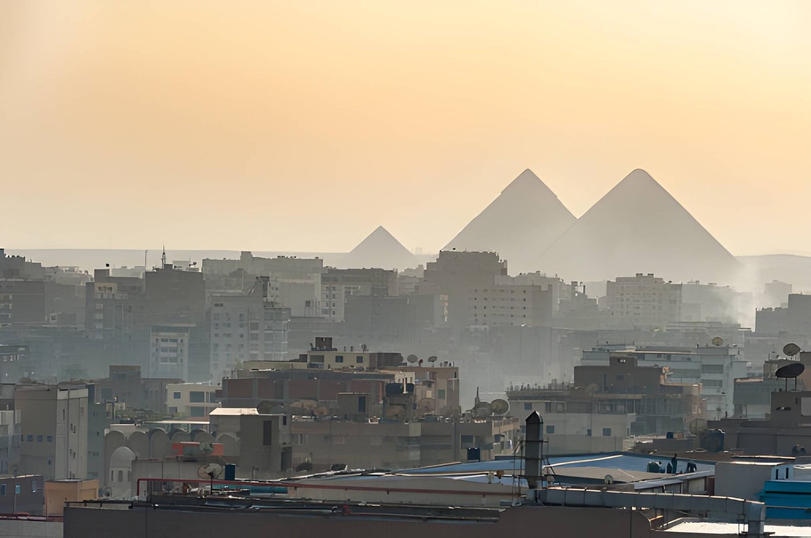 Giza city skyline with the Great Pyramids rising above Cairo buildings at sunset