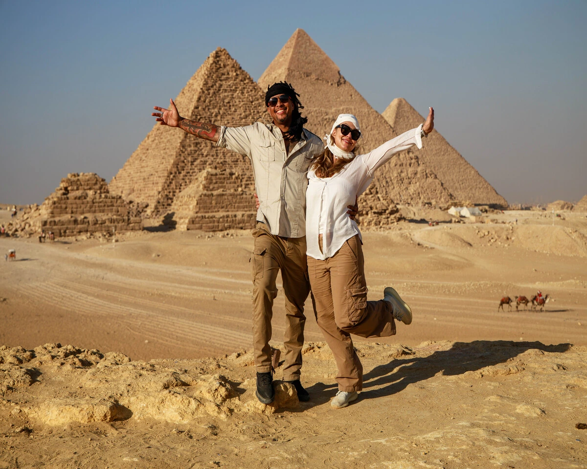 A couple taking photos with camels in front of the pyramids