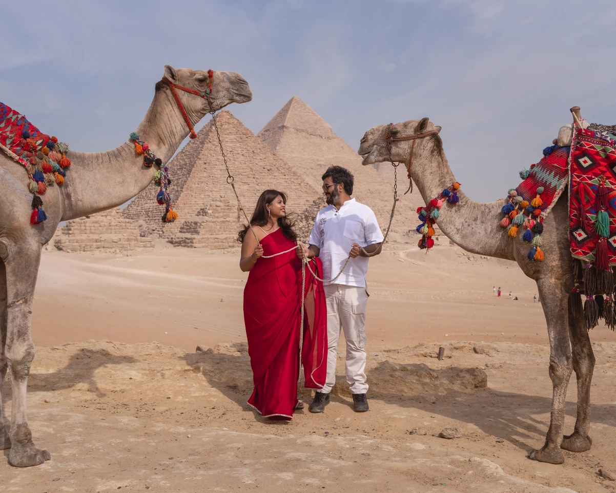 A couple taking photos with camels in front of the pyramids