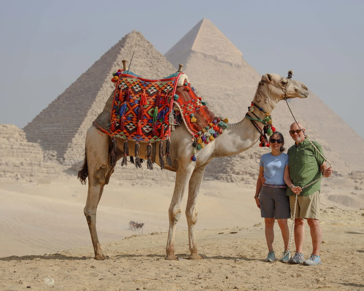 A couple taking photos with camels in front of the pyramids