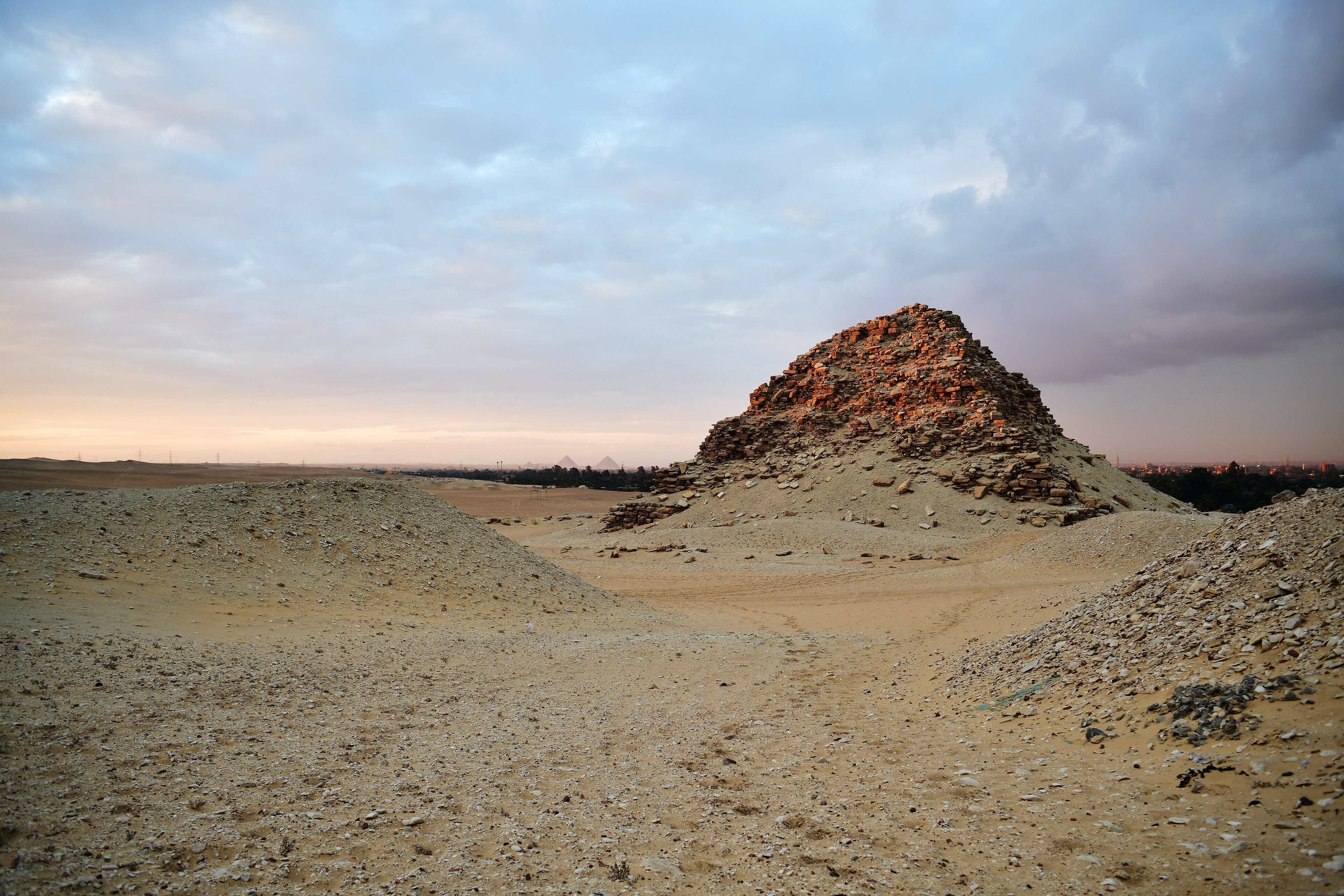 An ancient Egyptian pyramid at dusk with the Giza pyramids on the horizon